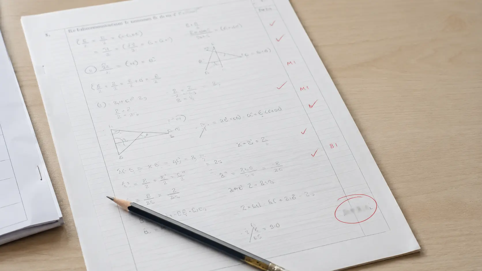 A marked GCSE past paper on a desk with the mark total circled in red and a pencil resting beside it